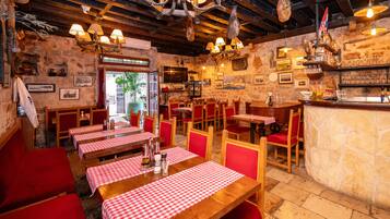 A rustic restaurant with wooden tables and red chairs, stone walls, and a bar area.