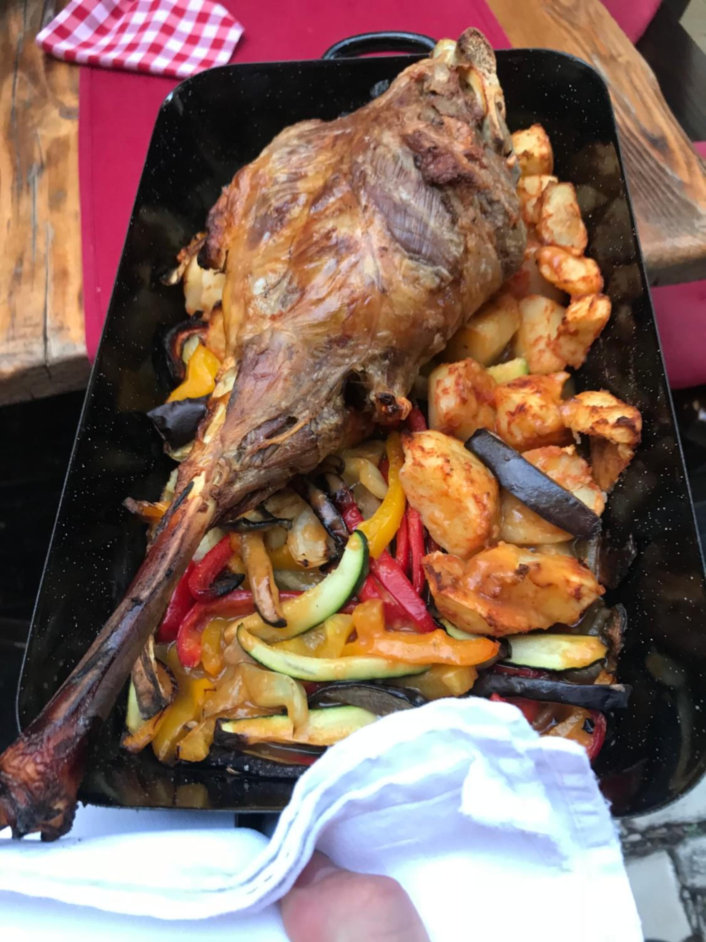 A roasted leg of lamb with vegetables on a black tray.