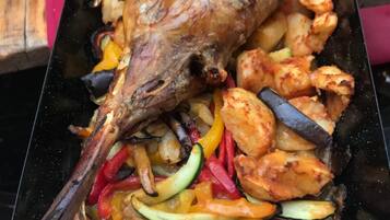 A roasted leg of lamb with vegetables on a black tray.
