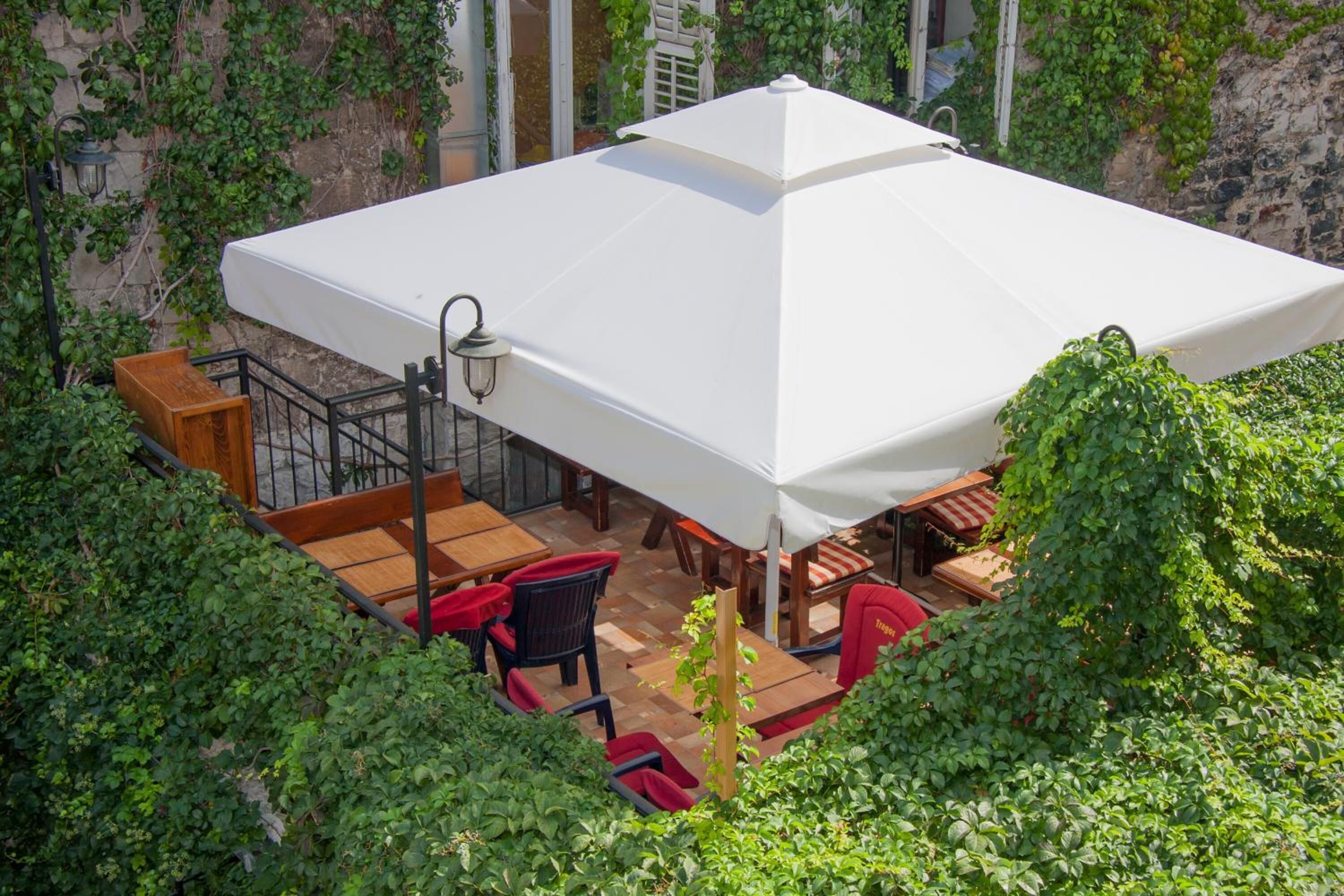 An outdoor patio with a white umbrella, wooden furniture, and a stone wall with greenery.