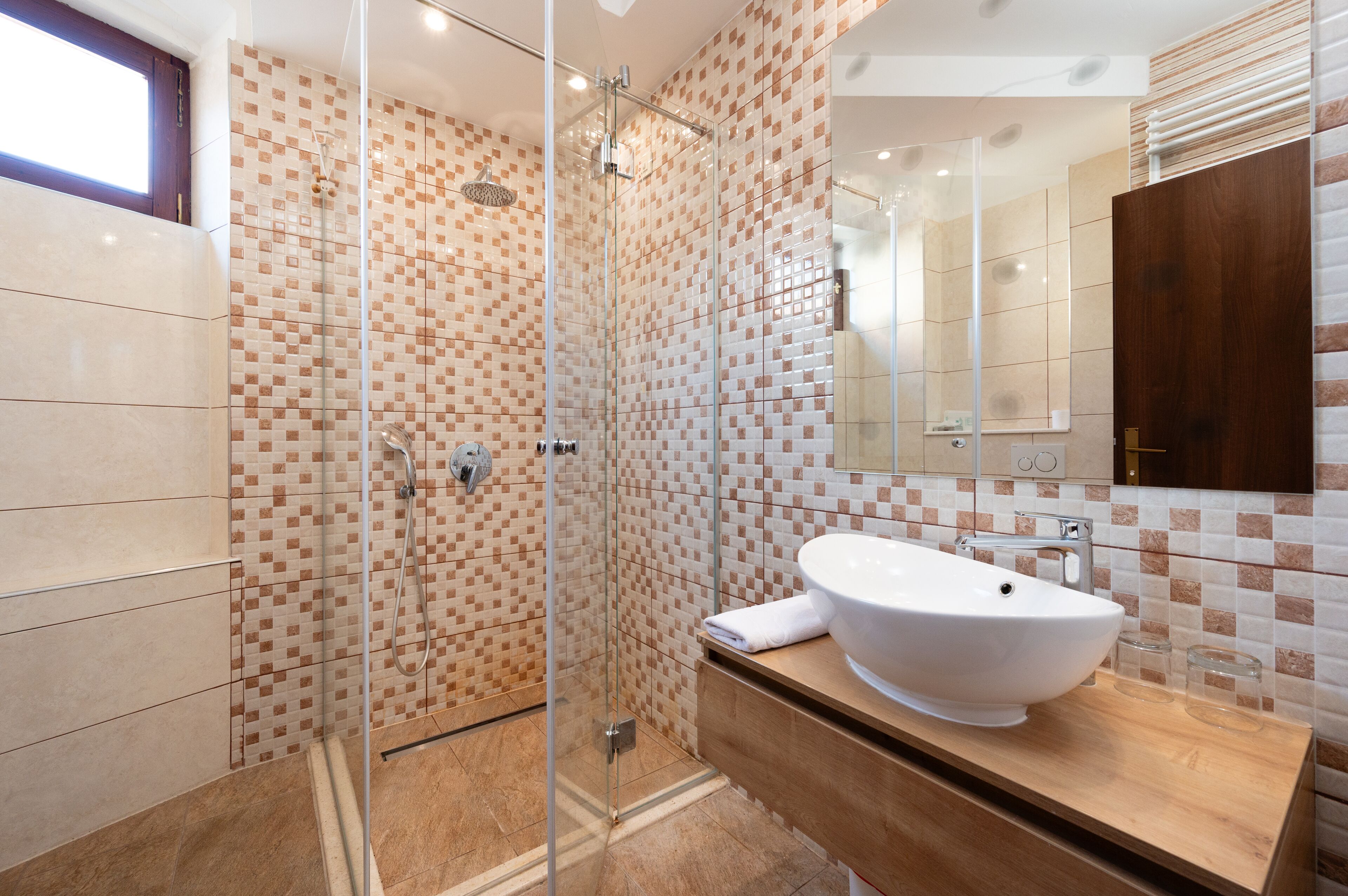 Un baño moderno con ducha de vidrio, un lavamanos grande de color blanco y un mueble de tocador de madera.
