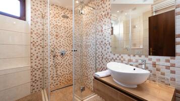 Un baño moderno con ducha de vidrio, un lavamanos grande de color blanco y un mueble de tocador de madera.