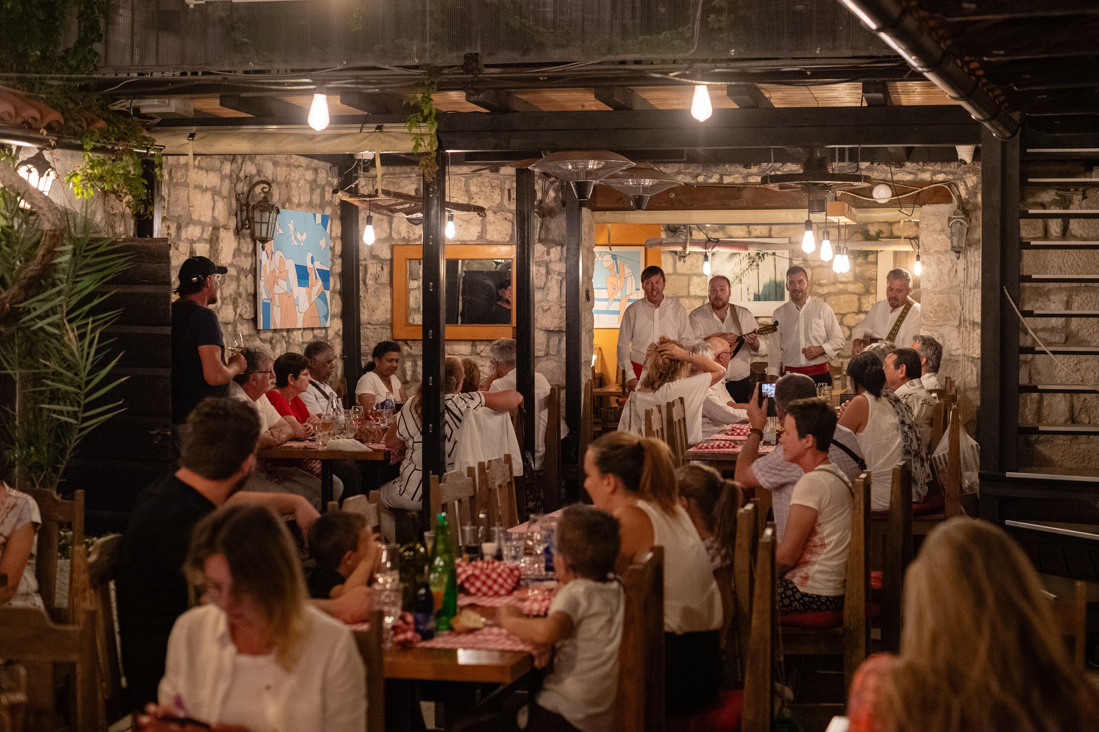 Un restaurante con paredes de piedra, vigas de madera y luces colgantes. Las mesas están cubiertas con manteles a cuadros rojos y blancos.