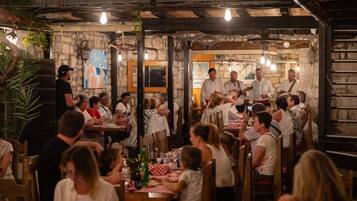 Un restaurante con paredes de piedra, vigas de madera y luces colgantes. Las mesas están cubiertas con manteles a cuadros rojos y blancos.