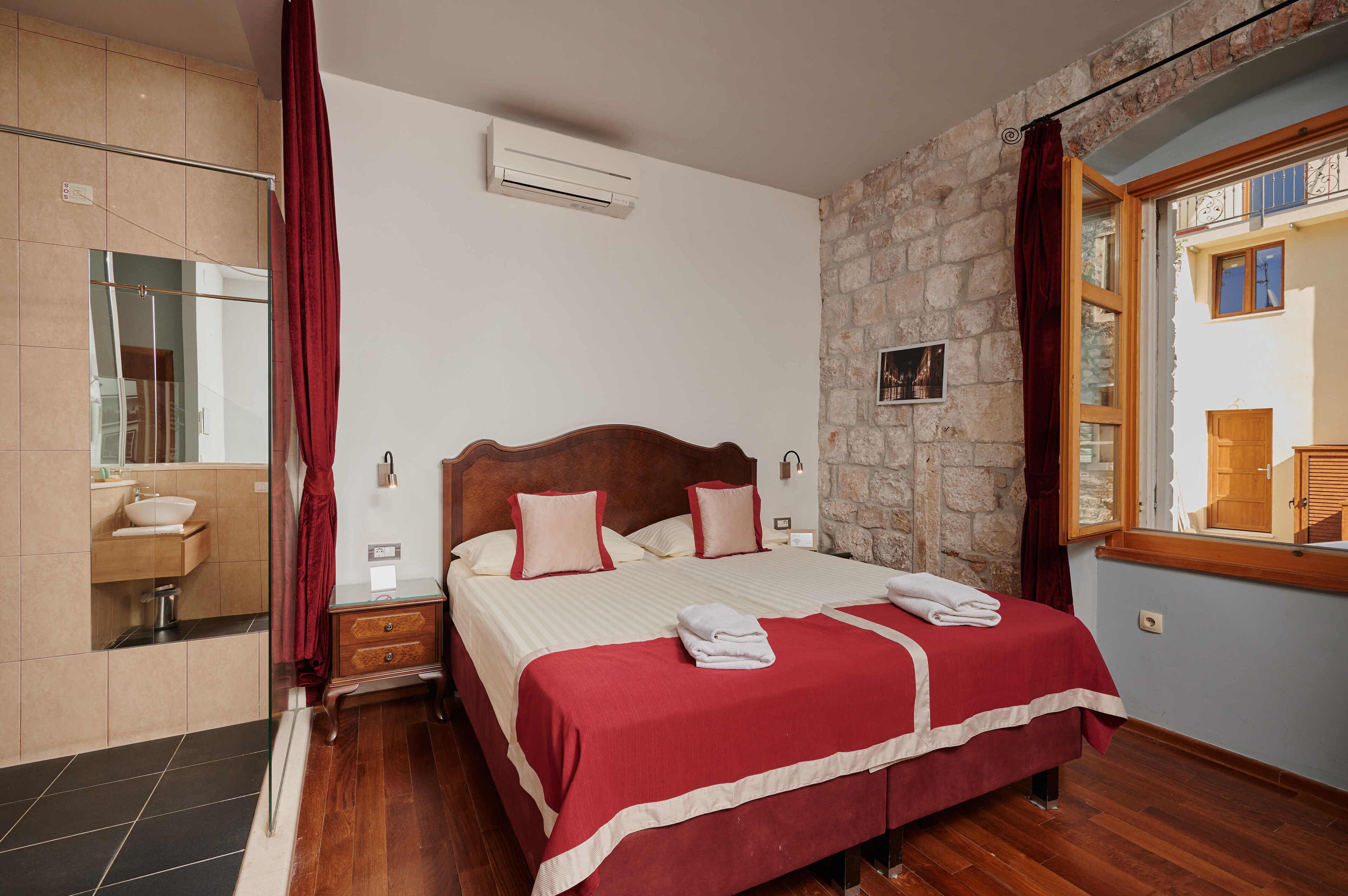 A hotel room with a large bed, a wooden headboard, a stone wall, and a window with curtains.