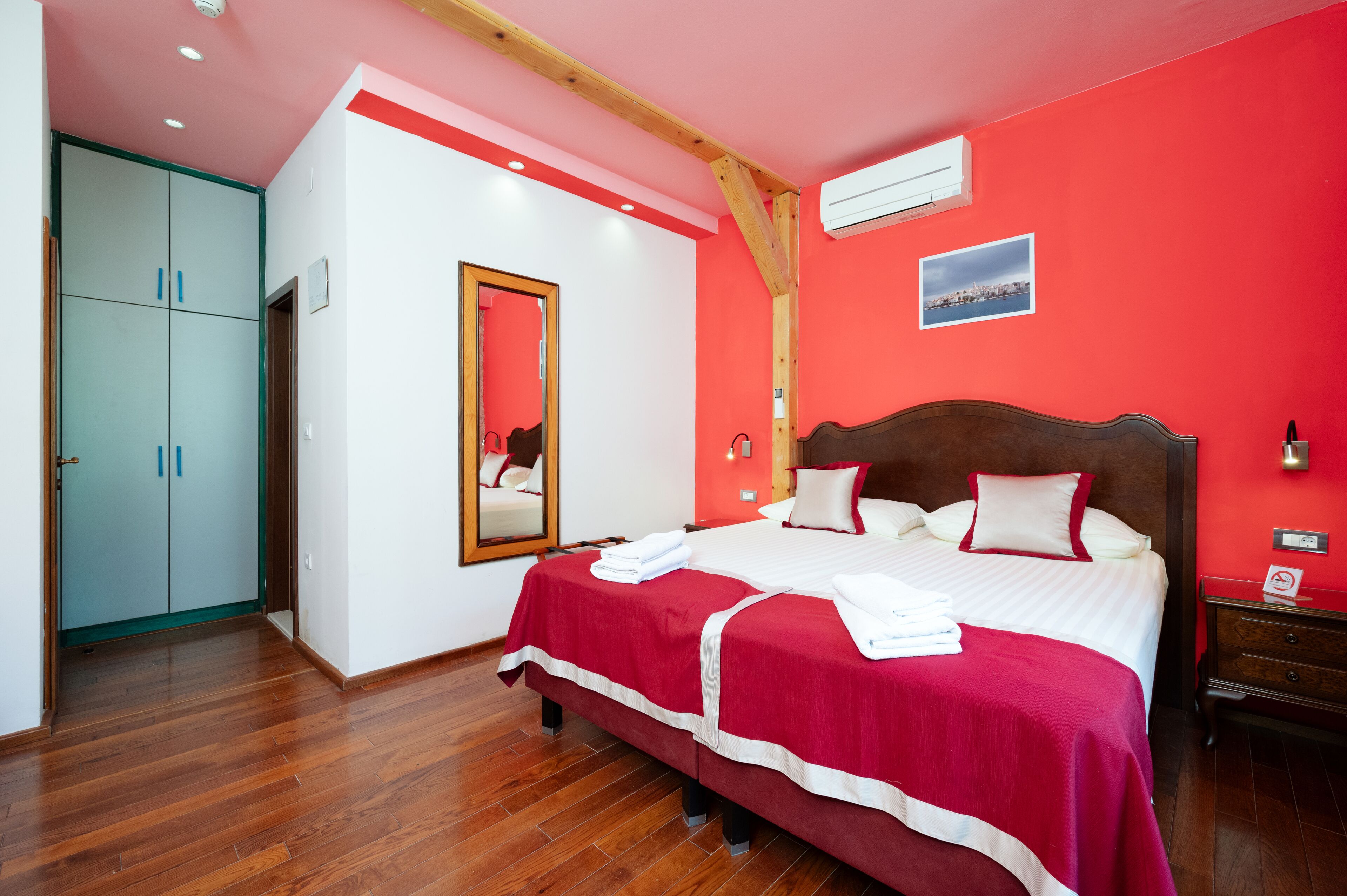 A bedroom with a large bed, a wardrobe, a mirror, and a picture on the wall.