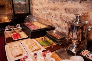 Egy svédasztal, amelyen különféle ételek találhatók, többek között hot dog, egy húsételekkel kínáló pult és egy sajtpult.
