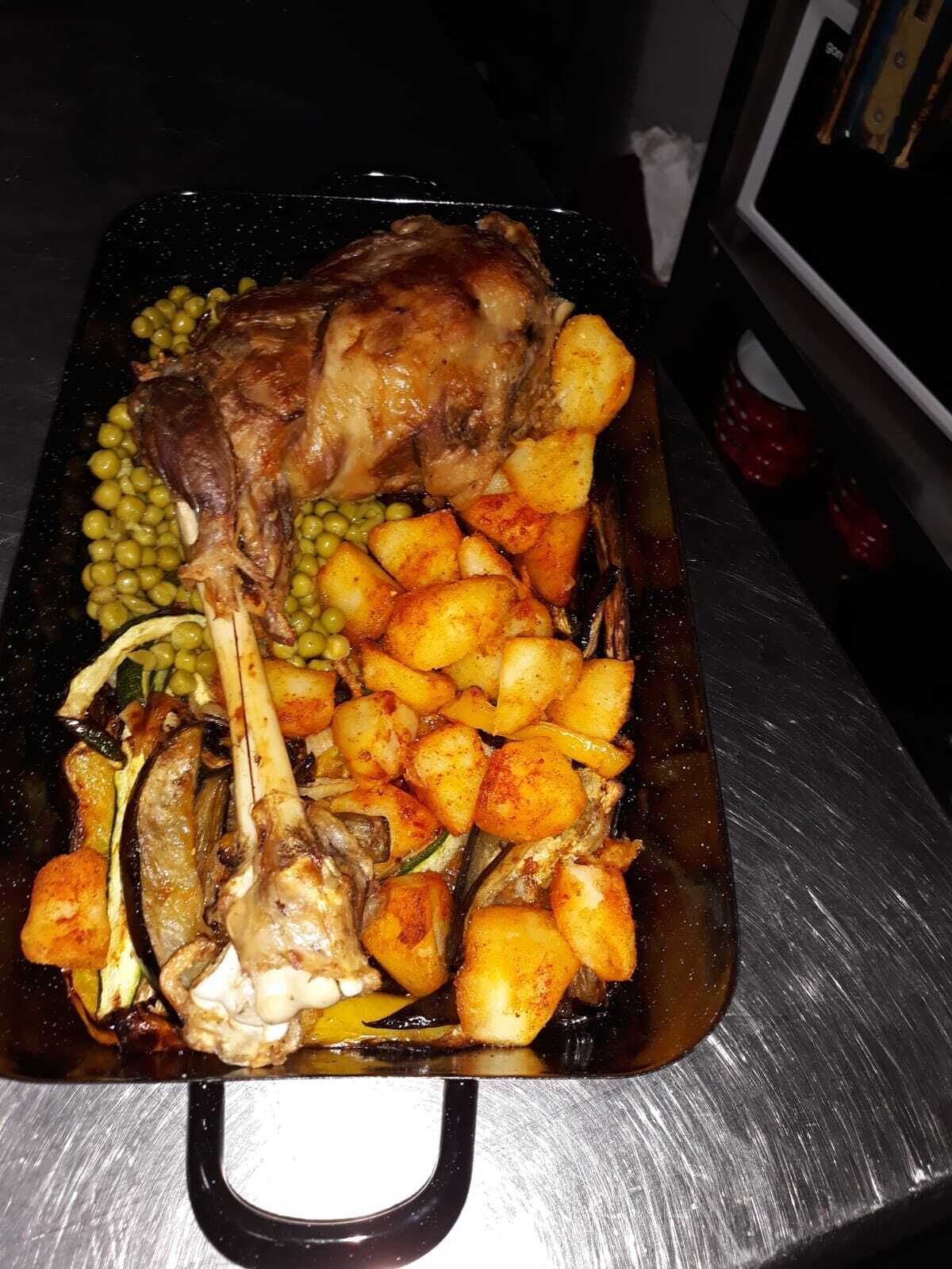 A roasted leg of lamb with potatoes and peas on a baking tray.