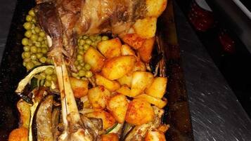 A roasted leg of lamb with potatoes and peas on a baking tray.