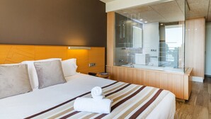 Habitación de hotel con una cama grande, cabecero de madera, box de ducha de vidrio y vistas al baño.