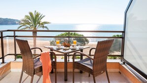 Un balcón con sillas de mimbre, una mesa con alimentos para el desayuno y vistas al mar.