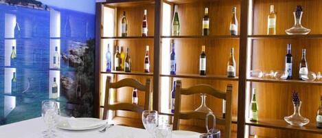 A restaurant interior with a long table set for dining, wooden shelves with wine bottles, and a mural on the wall.