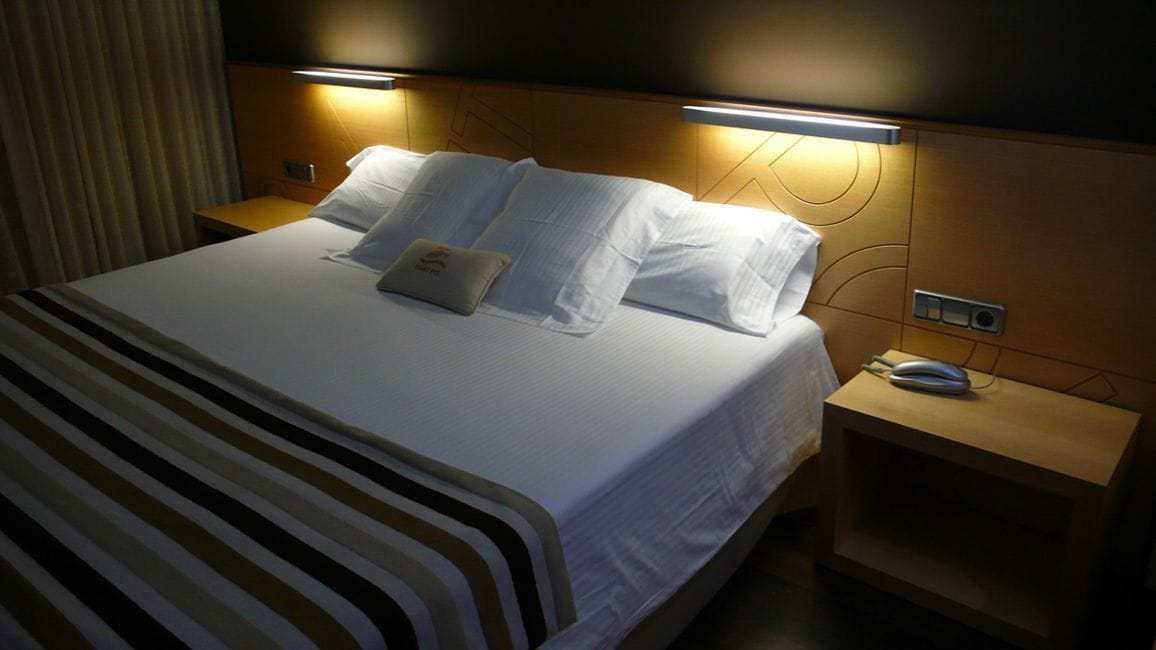A hotel room with a neatly made bed, two bedside tables, and a nightstand with a phone.