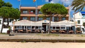 Un restaurante frente a la playa con mesas al aire libre, un letrero que indica que es restaurante y banderas en el techo.