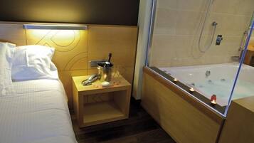 Una habitación de hotel con cama, mesita de noche y bañera con mampara de vidrio.