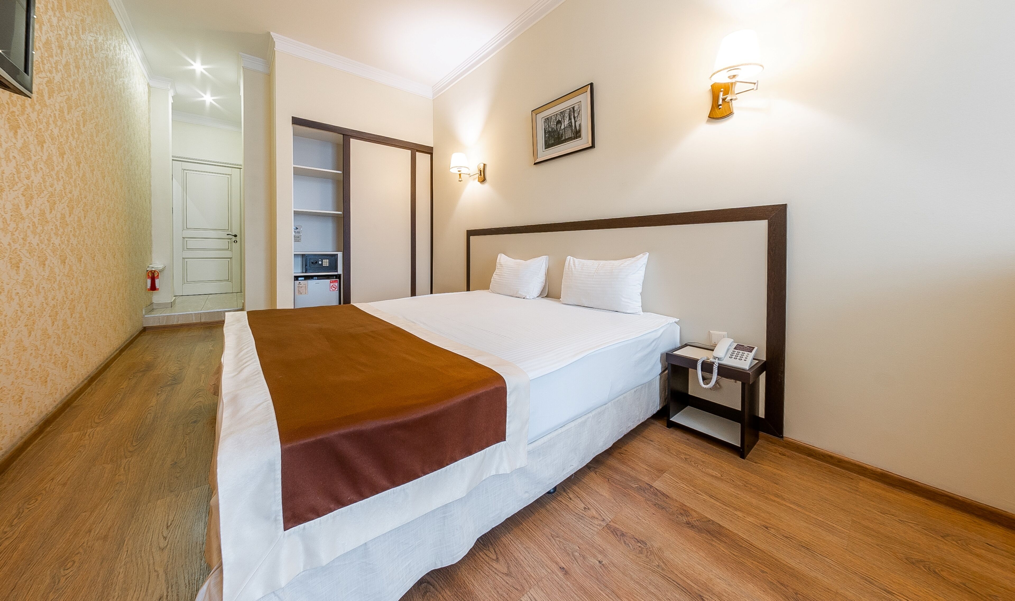 Habitación de hotel con cama, mesita de noche y lámpara de pared.