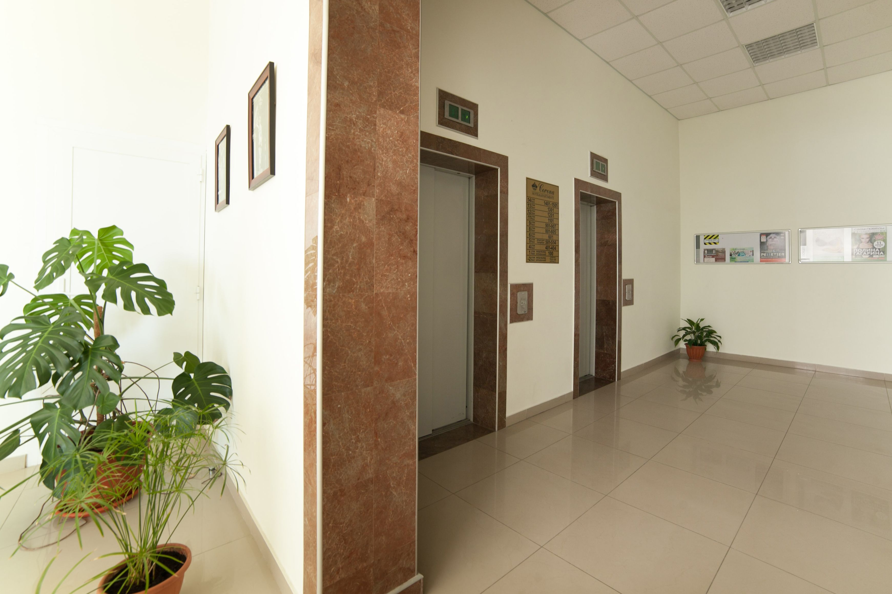 A clean, well-lit hallway with potted plants, doors, and informational posters on the walls.