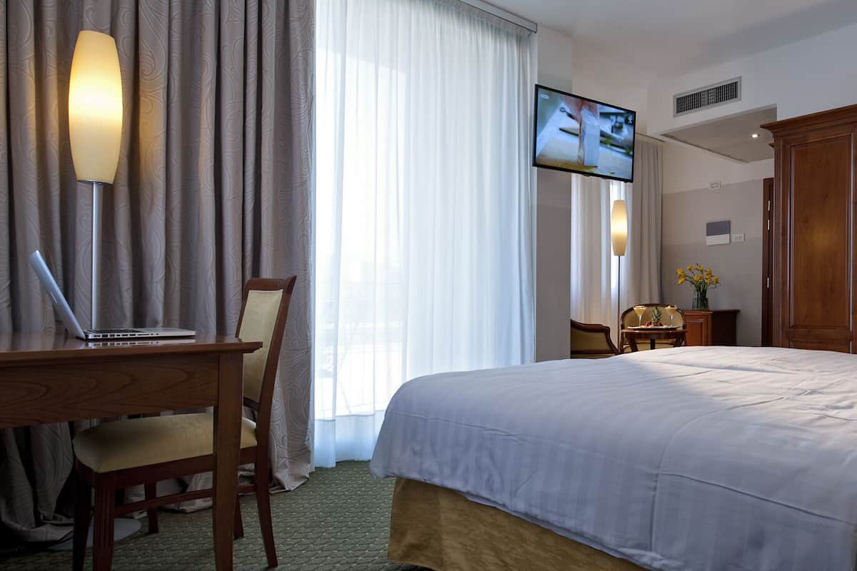 Ein Hotelzimmer mit Bett, Schreibtisch mit Laptop, Stuhl, Wandfernseher und Holzschrank.