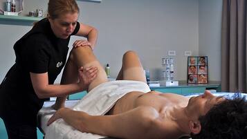 A massage therapy session in a room with a massage table, a towel, and a shelf with various items.