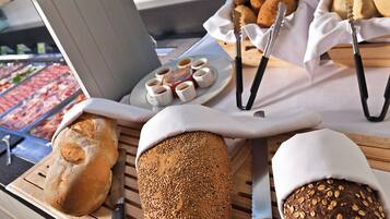 A variety of breads and pastries on a wooden table, with a meat display in the background.