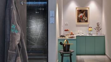 Un baño moderno con puerta de vidrio, un perchero, un lavamanos con juego de té y un cuadro en la pared.