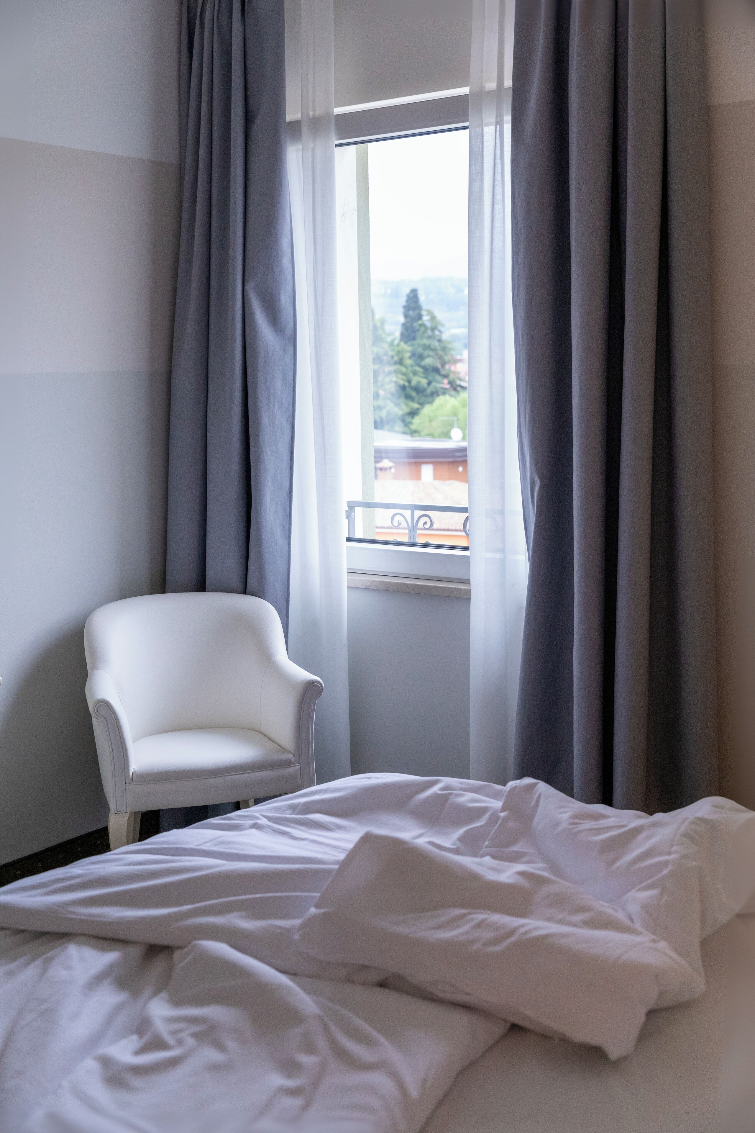 A room with a bed, a chair, and a window with curtains.