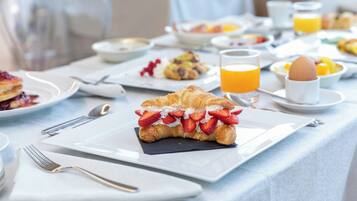 Ein Frühstückstisch mit Croissants, Obst und Orangensaft.