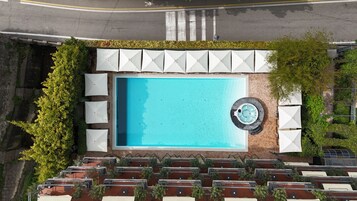 Vista aérea de una piscina en la azotea con jacuzzi, rodeada de mobiliario exterior y vegetación.