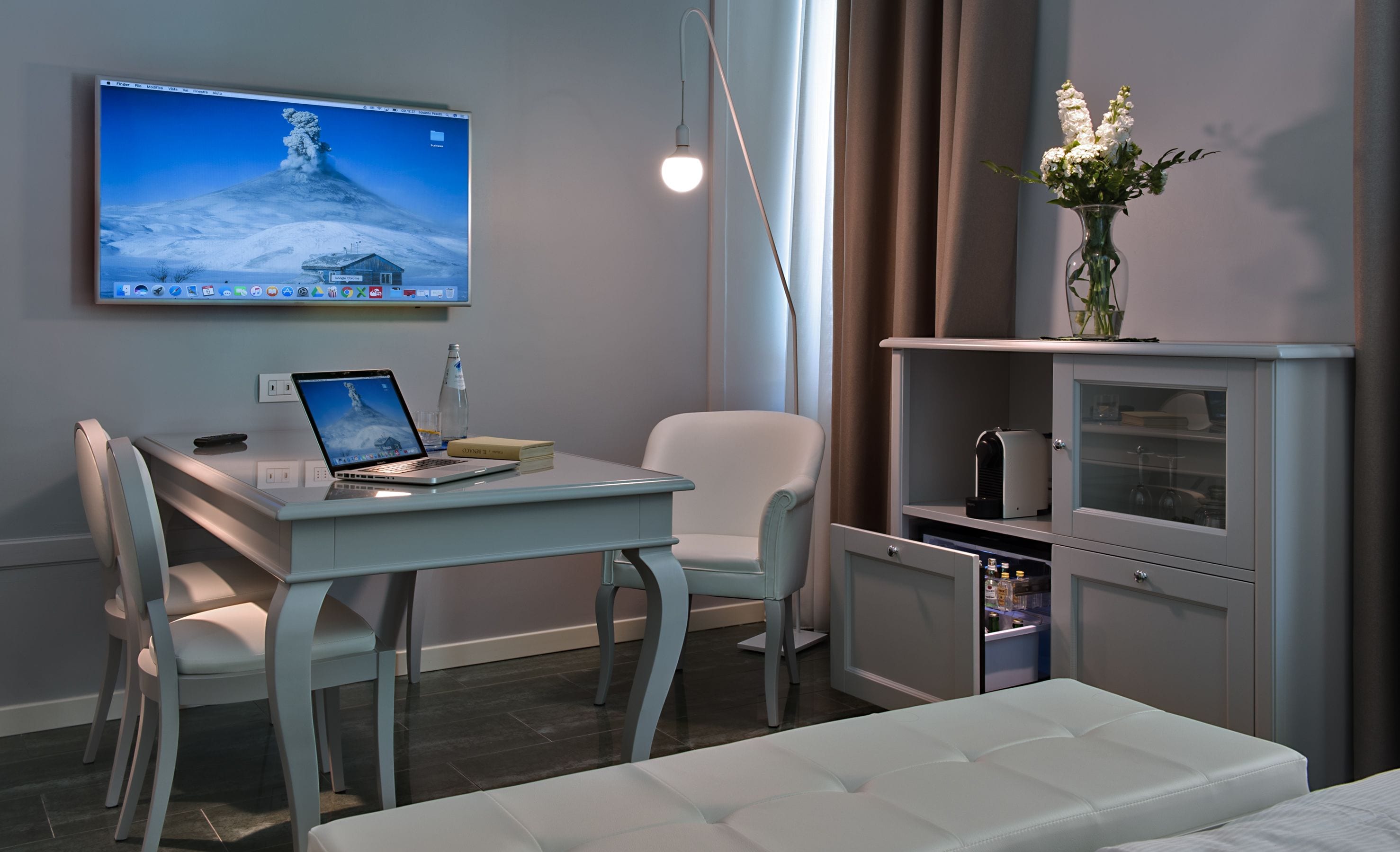 A modern hotel room with a desk, chair, laptop, and a bed.