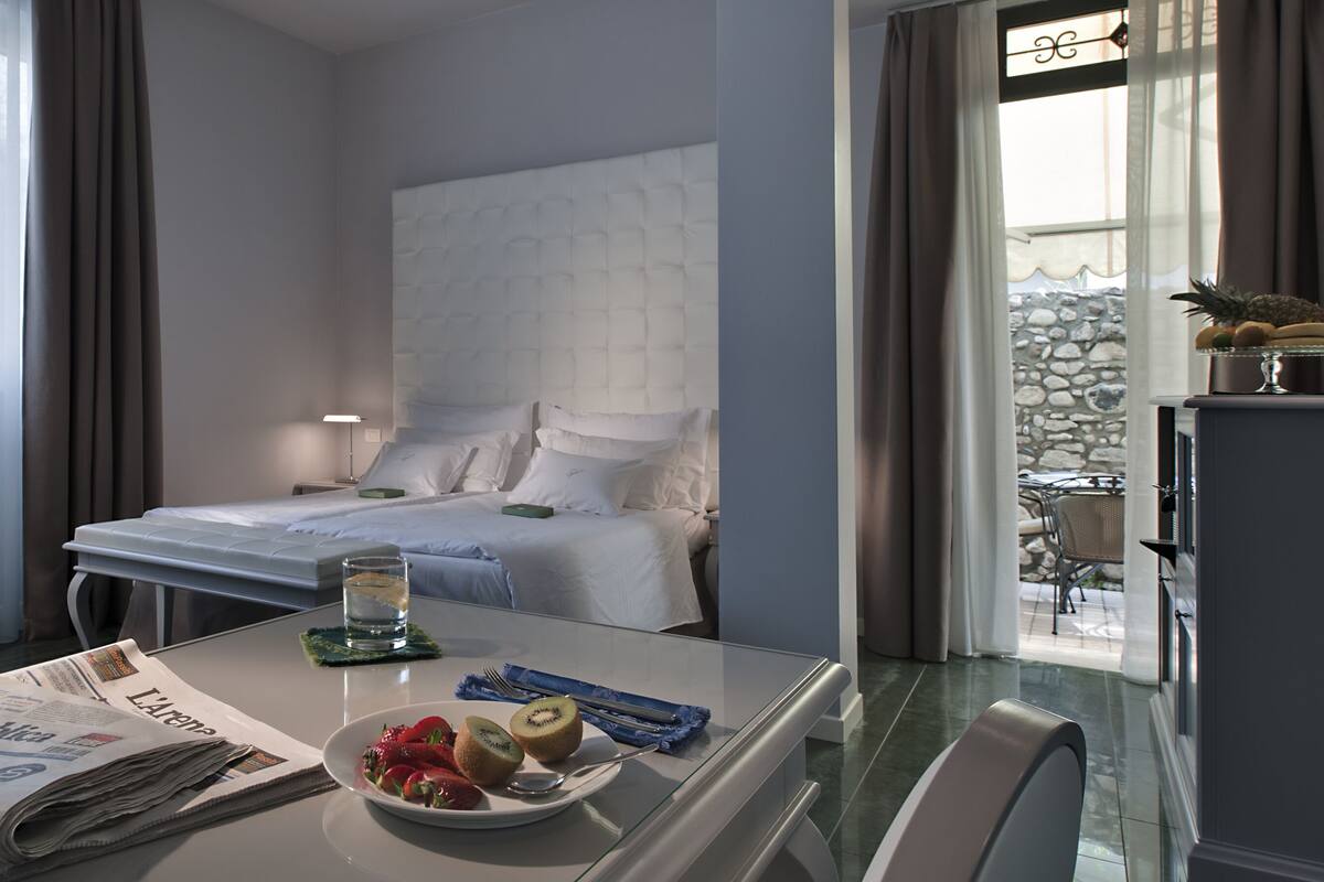 Ein Hotelzimmer mit einem Bett, einem Esstisch mit Frühstück, einem Stuhl und einer Zeitung.