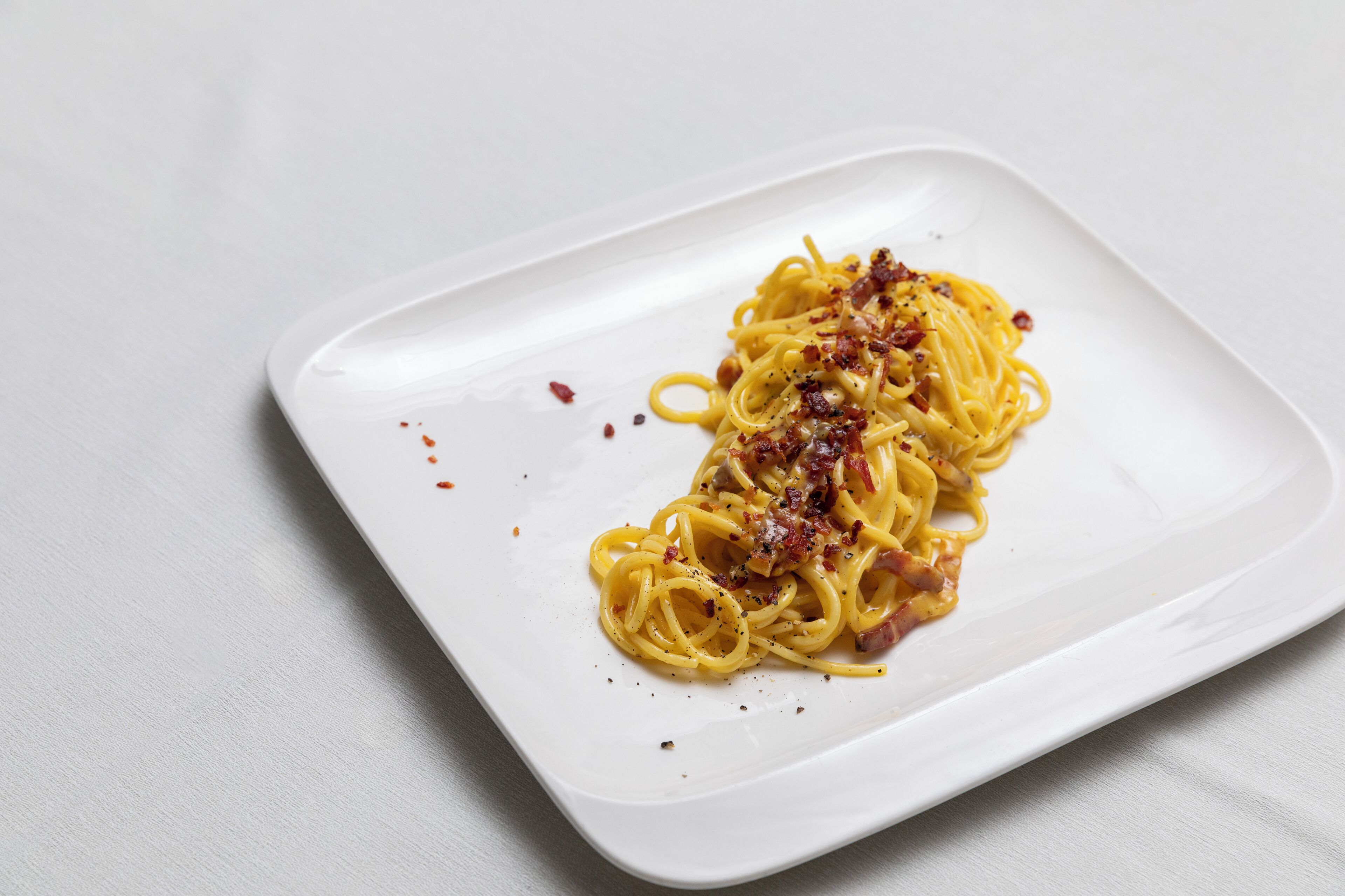 A plate of spaghetti with bacon and cheese on a white plate.