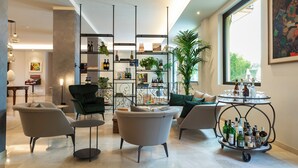 Een moderne woonkamer met een bank, fauteuils, een salontafel en een boekenplank vol boeken en decoratieve objecten.