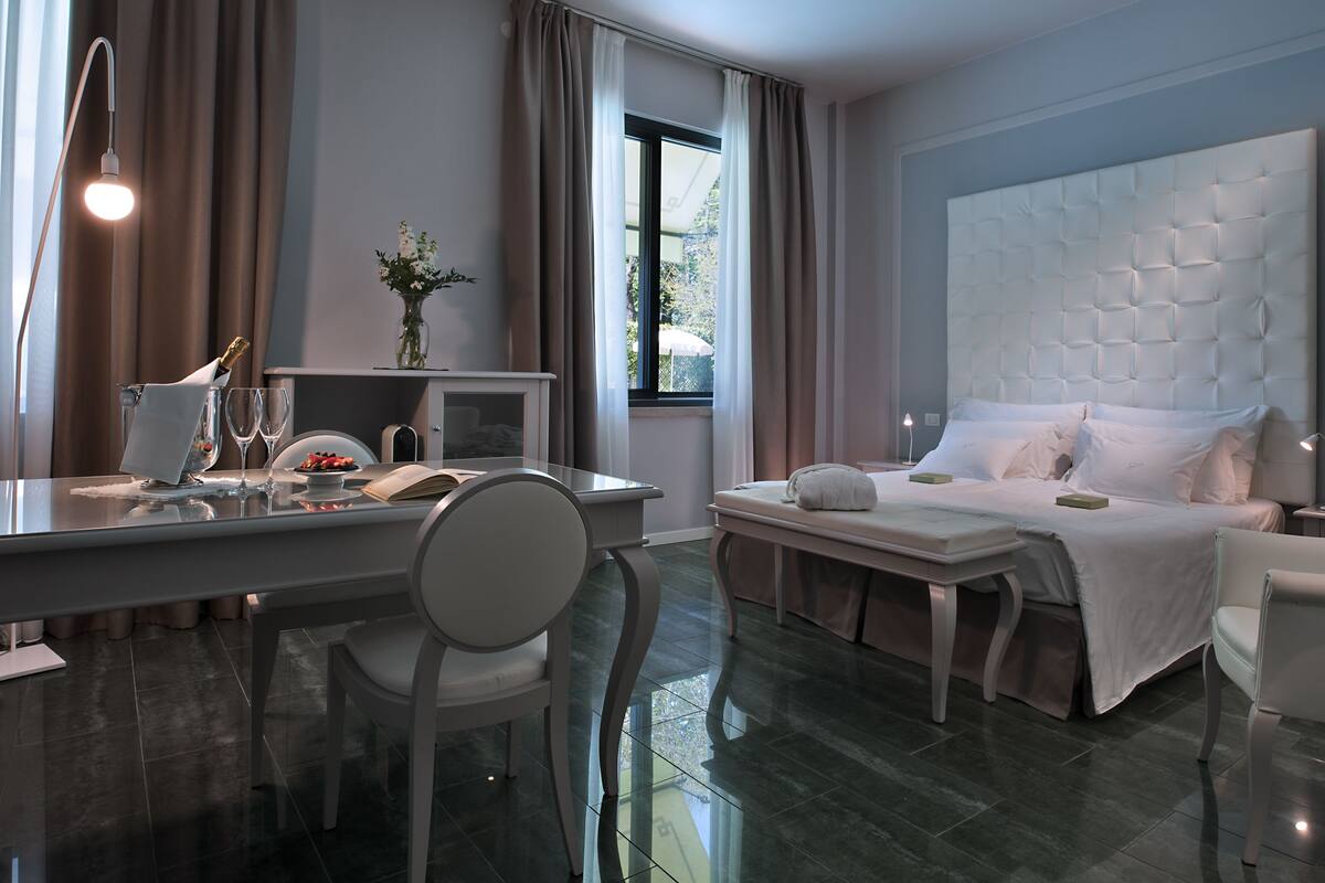 Ein modernes Hotelzimmer mit einem großen Bett, einem Schreibtisch mit Stuhl, einem Nachttisch und einem Fenster mit Vorhängen.