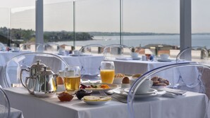 Een ontbijttafel gedekt met ontbijtartikelen, waaronder een theepot, kopjes en een glas sinaasappelsap, met uitzicht op een schilderachtig landschap.