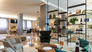 Een ruime hotel lobby met een modern design, met een groot zitgedeelte met banken en fauteuils, een houten salontafel en een wijnrek.