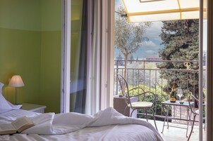 Habitación de hotel con cama, lámpara de lectura, balcón con mesa y sillas, y una botella de champán.