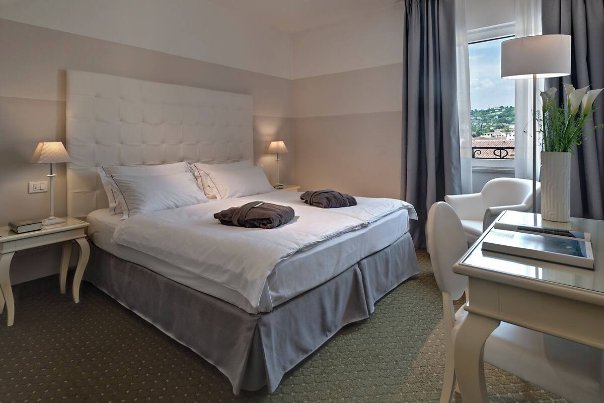 Ein Hotelzimmer mit Bett, Nachttischen, einem Schreibtisch und Blick ins Freie.