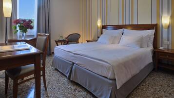 Une chambre d’hôtel avec un grand lit, un bureau et une chaise. Un vase rempli de fleurs est posé sur le bureau.