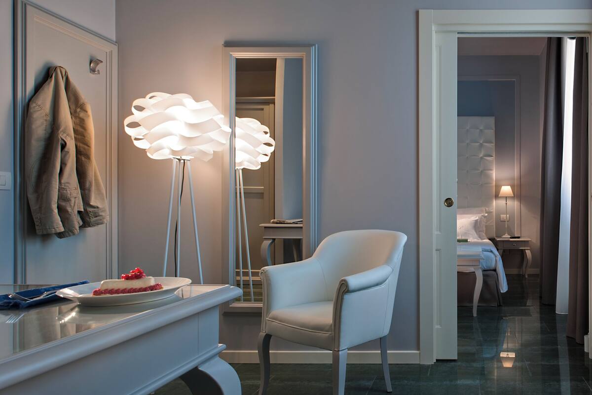 Ein modernes Hotelzimmer mit einem weißen Sessel, einem großen Spiegel und einer Stehlampe.