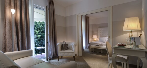 Habitación de hotel con cama, zona de estar con sillón, escritorio con lámpara y vistas al exterior.