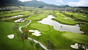 A golf course with multiple bunkers, water hazards, and a clubhouse in the background.