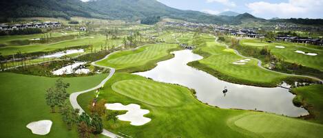 Campo de golf con numerosos búnkeres, zonas de agua y un club de campo al fondo.