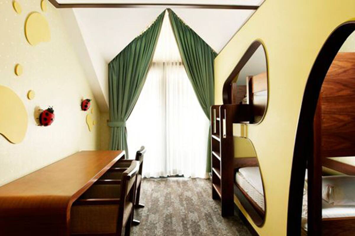 Une chambre avec un lit superposé, un bureau et une chaise. Il y a des rideaux et une fenêtre donnant sur un beau paysage.