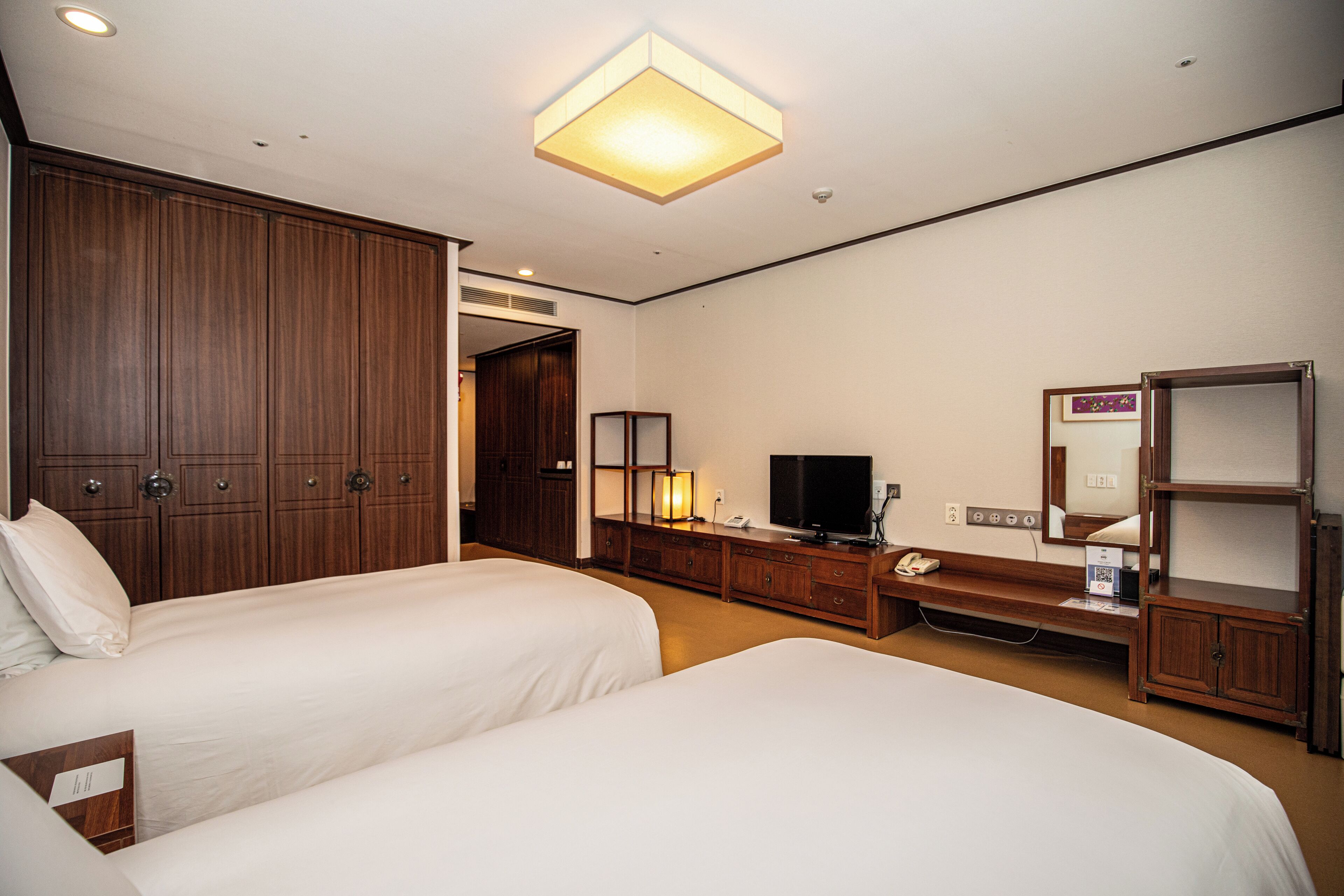 Une chambre d’hôtel avec deux lits, une armoire en bois, un bureau avec une télévision et une table de chevet.