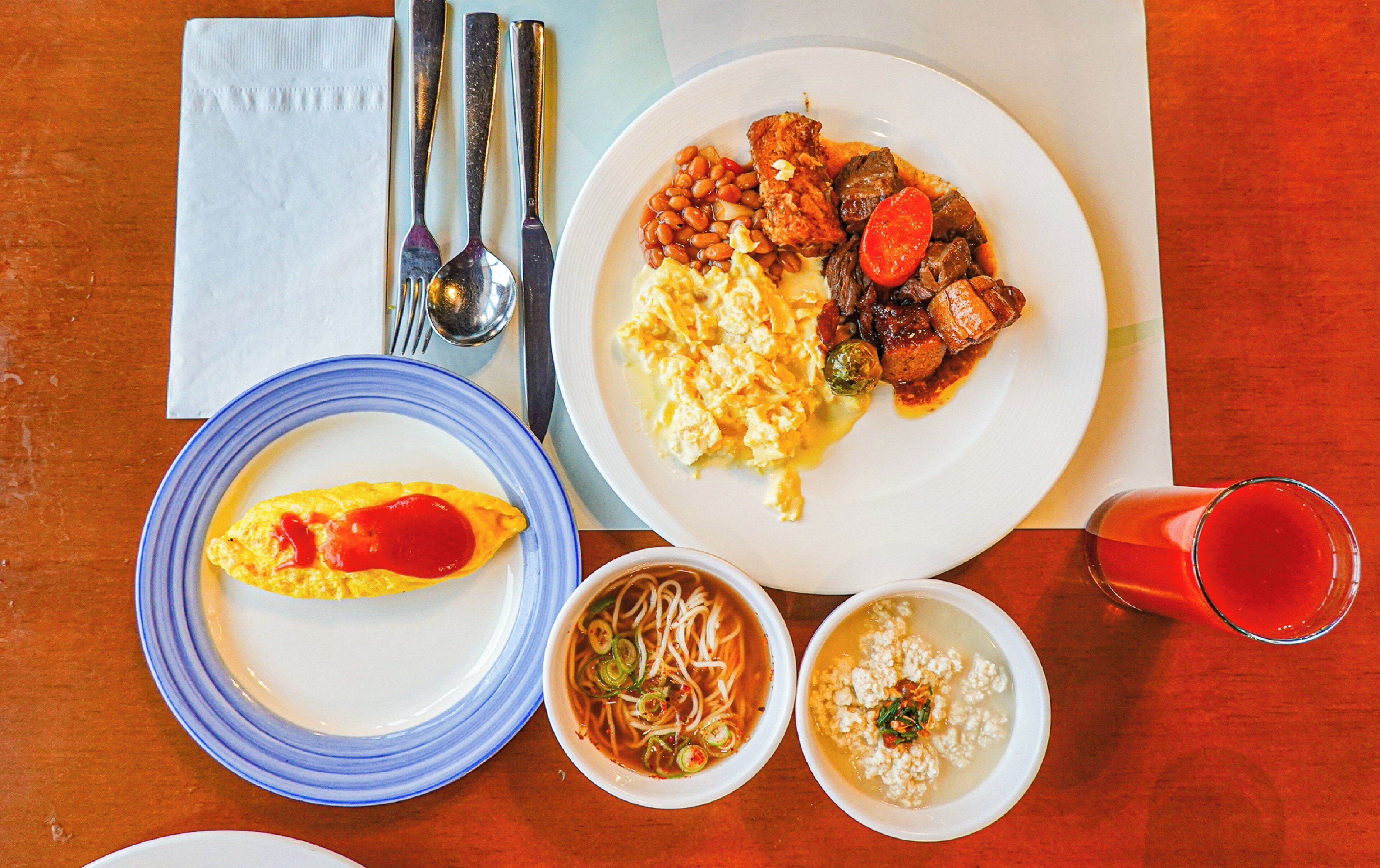 A table with plates of food, a glass of red drink, and a napkin with cutlery.