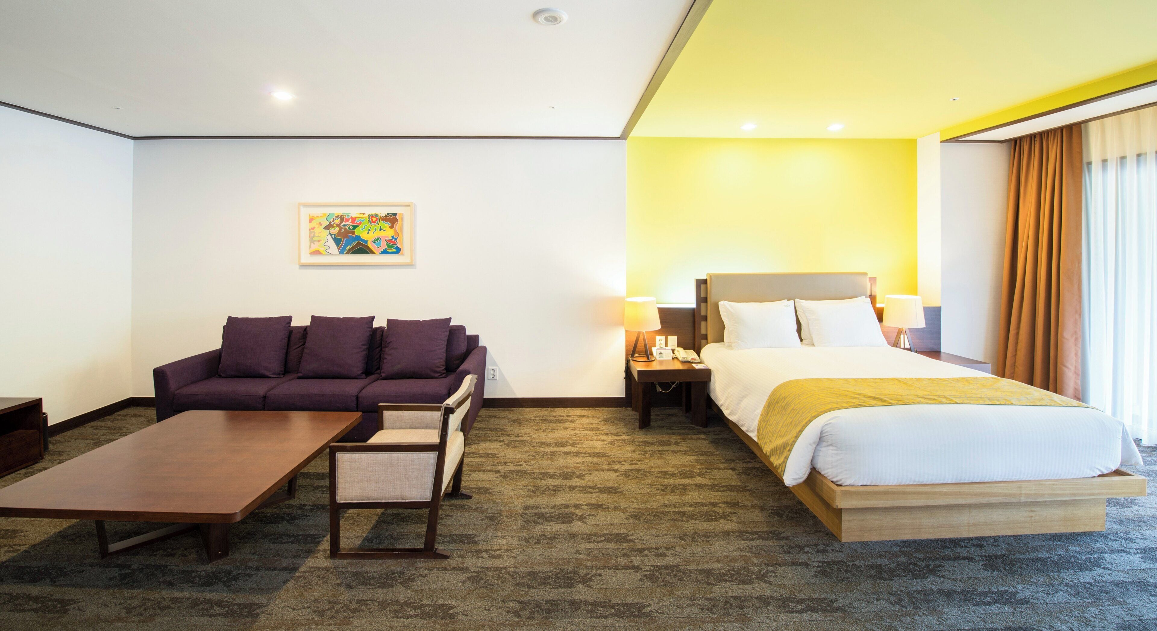 A hotel room with a bed, a sofa, a coffee table, and a nightstand with a lamp.