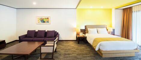A hotel room with a bed, a sofa, a coffee table, and a nightstand with a lamp.