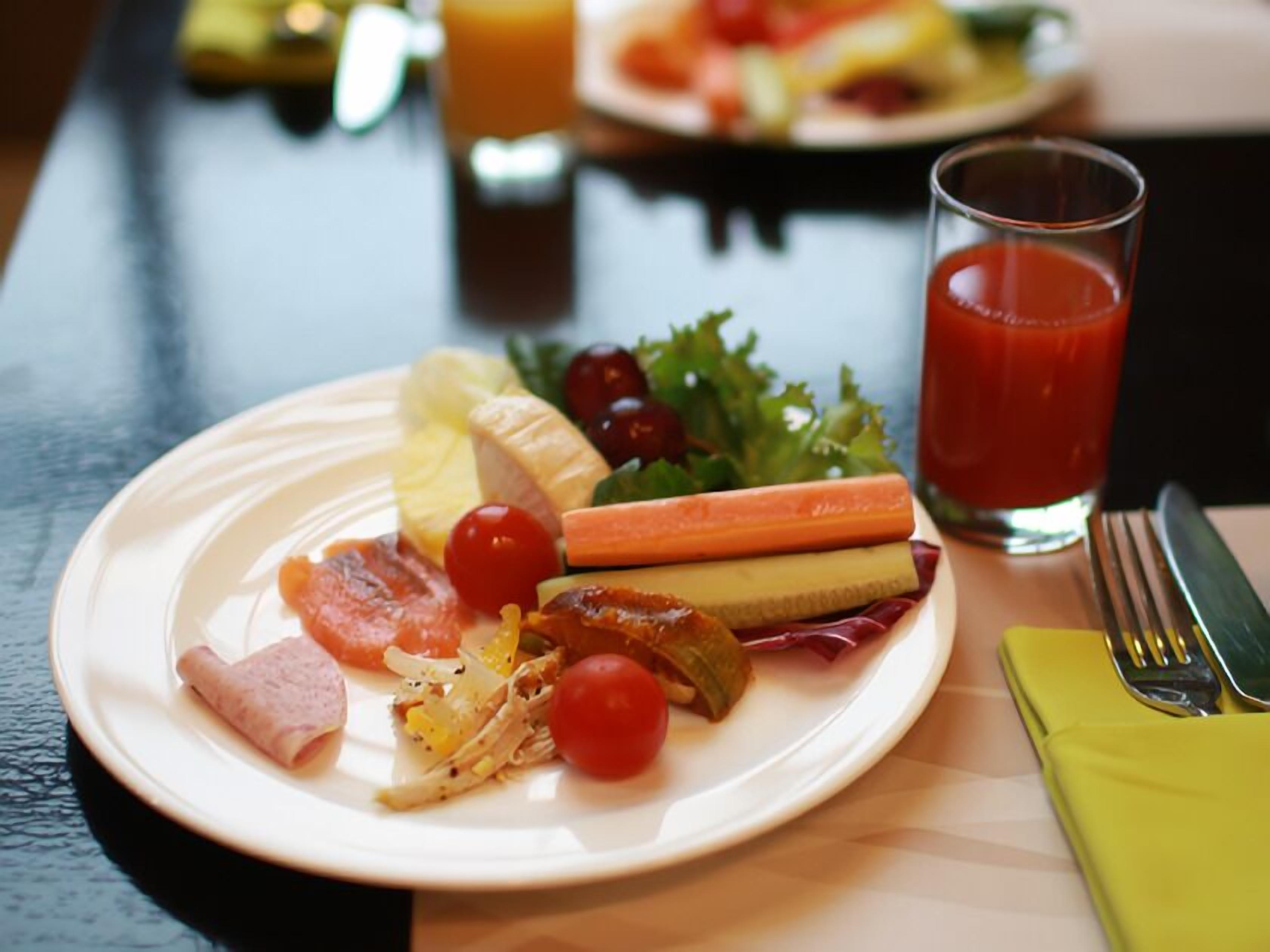 A plate of assorted food including ham, cheese, and vegetables, with a glass of tomato juice on a table.