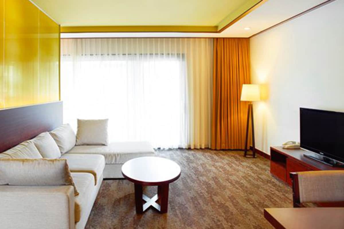 Een hotelkamer met een zithoek, een ronde salontafel, een televisie en een lamp.