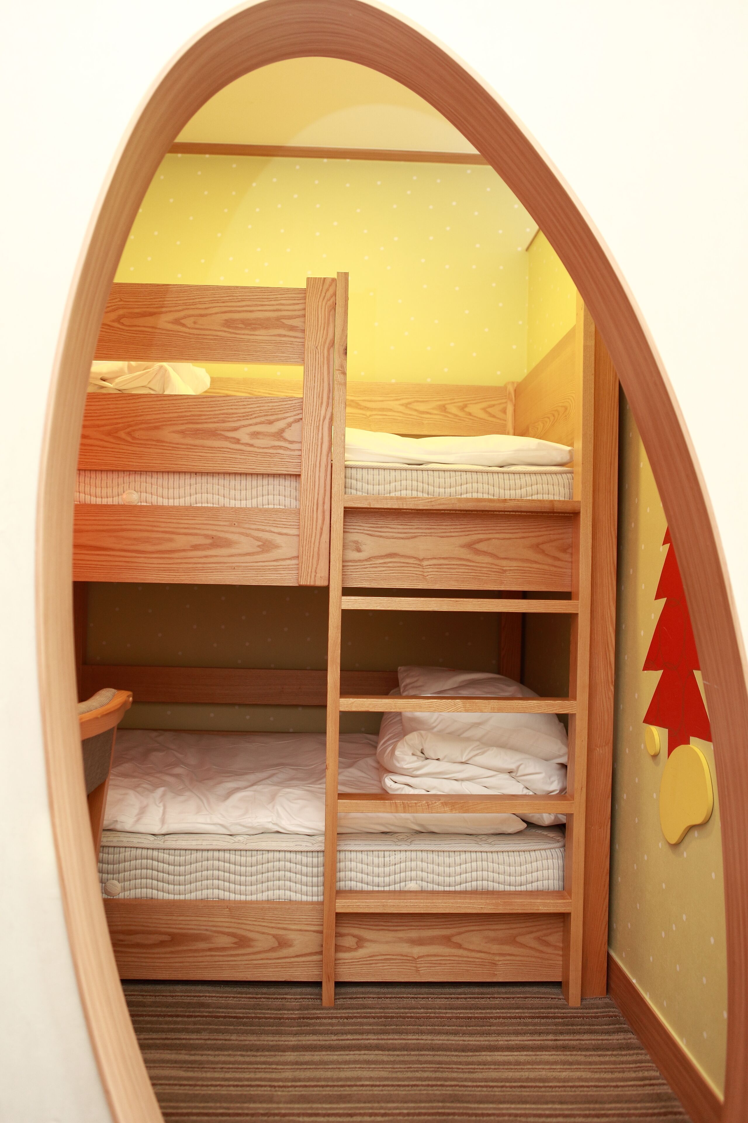Una cama litera con estructura de madera y una pared amarilla decorada con estrellas.